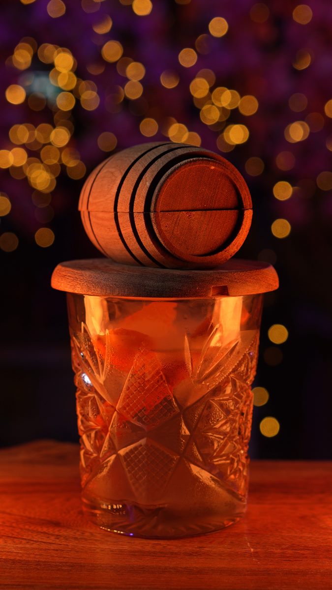 A smoked whiskey in a crystal glass topped with a miniature oak barrel