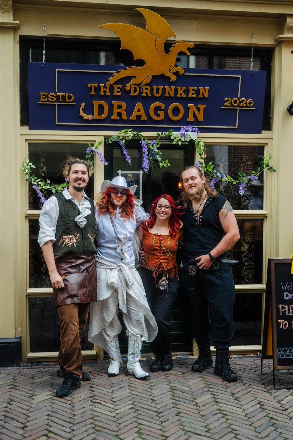 The four founders of The Drunken Dragon in costume outside the tavern, under its gold dragon sign